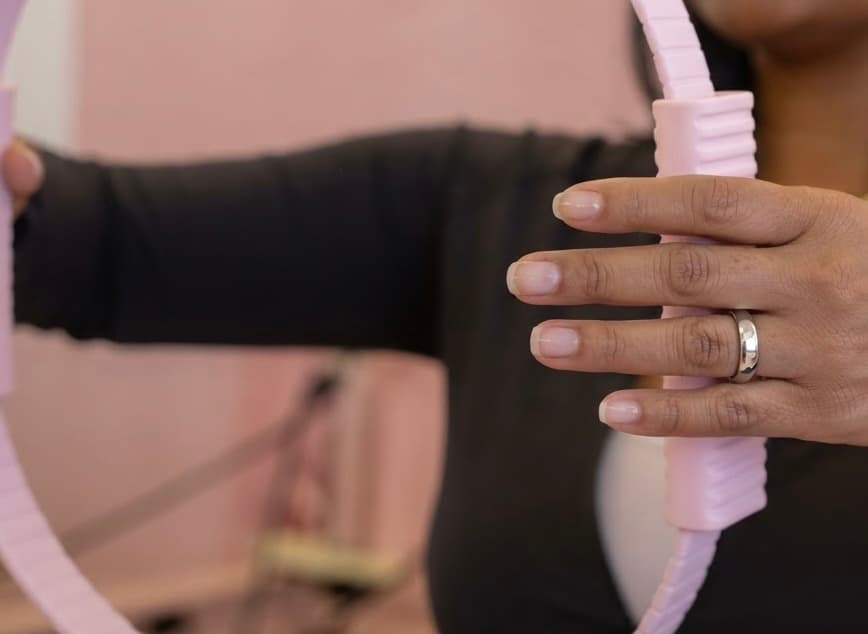Hands holding a pink Pilates ring during a Bloom 55+ class at Bloomhouse